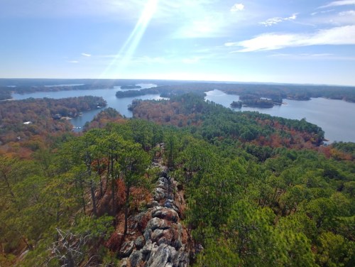 A scenic view from a rocky overlook, showcasing lakes and forested hills under a clear blue sky.