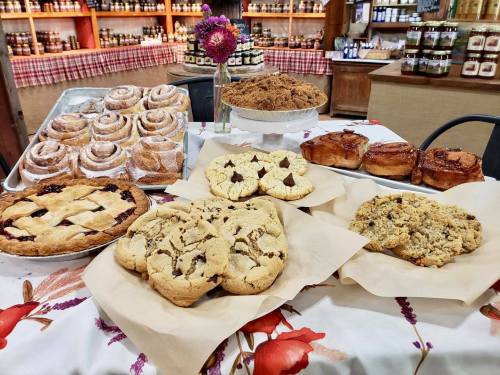 A display of various baked goods, including cookies, cinnamon rolls, and pies, on a floral tablecloth.