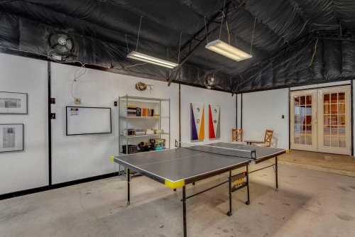 A spacious game room featuring a ping pong table, shelves with books, and double doors leading outside.