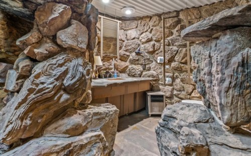A rustic bathroom with stone walls, a wooden counter, and unique rock formations creating a natural aesthetic.