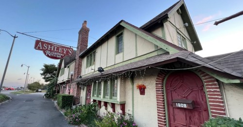 A charming restaurant exterior with a sign reading "Ashley's," featuring a brick and wood design at dusk.