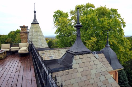 View of a rooftop with decorative spires and a wooden deck, surrounded by lush green trees.