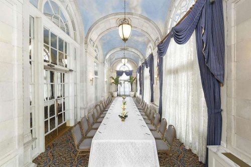 Elegant dining room with a long table set for a formal event, featuring large windows and decorative curtains.