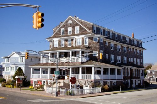 Historic building with multiple stories, a wraparound porch, and a traffic light in front against a clear blue sky.