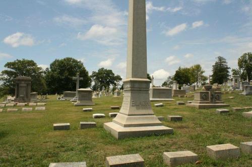 A cemetery scene featuring gravestones and monuments under a blue sky with scattered clouds.