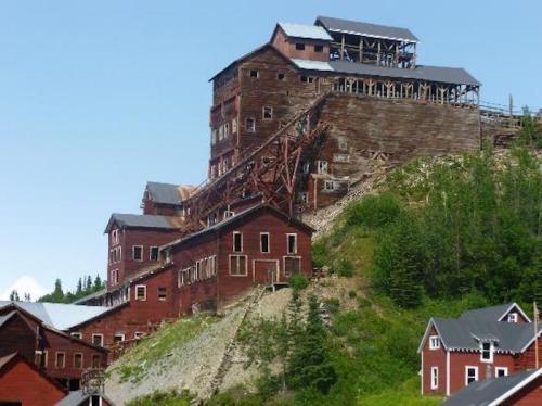 Historic mining buildings on a hillside, featuring red wooden structures and a steep incline under a clear blue sky.