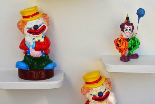 Colorful clown figurines displayed on white shelves, featuring playful designs and cheerful expressions.
