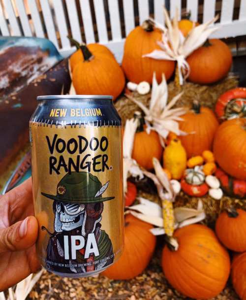 A hand holds a Voodoo Ranger IPA can in front of a display of pumpkins and autumn decorations.