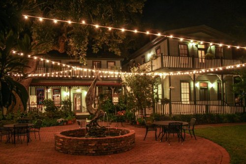 A charming two-story house at night, adorned with string lights, surrounded by a cozy courtyard and seating area.