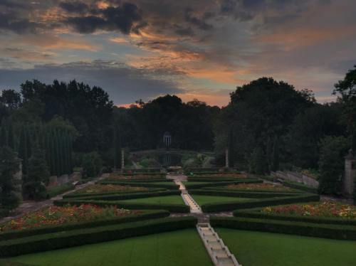 A serene garden at sunset, featuring neatly trimmed hedges, colorful flowers, and a cloudy sky.