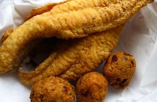 Fried catfish fillets with golden-brown hushpuppies on a white paper background.