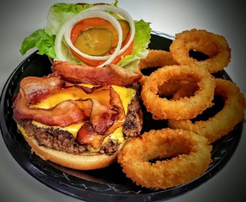A juicy cheeseburger topped with bacon, lettuce, tomato, and pickles, served with crispy onion rings on the side.
