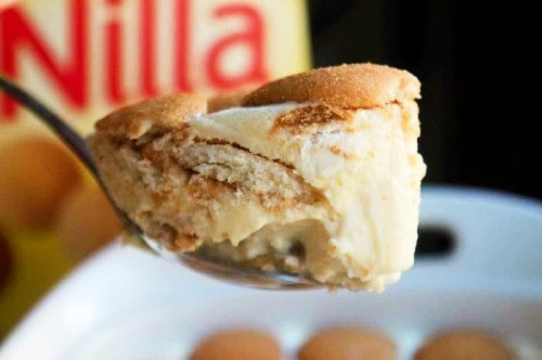 A spoonful of creamy dessert layered with vanilla wafers and a smooth filling, with a box of Nilla wafers in the background.