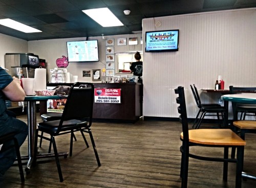 Interior of a casual dining restaurant with tables, chairs, and a counter displaying a menu and promotional signs.