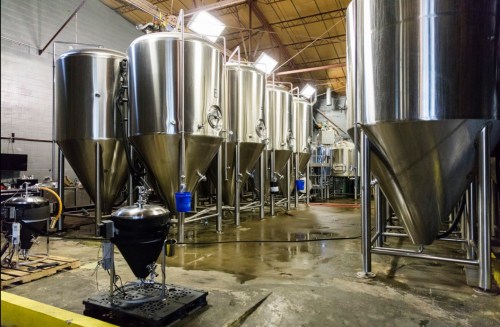 A brewery interior featuring several large stainless steel fermentation tanks and brewing equipment.