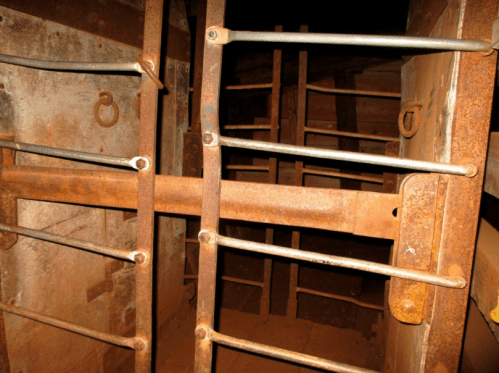 Rusty metal bars and rods create a grid-like structure in a dimly lit, industrial space.