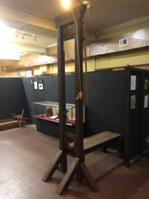 A wooden guillotine displayed in a museum, with a light above and dark walls in the background.