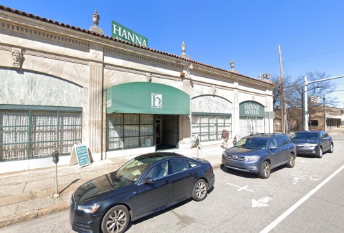 A storefront with "Hanna" signage, green awning, and parked cars on a sunny day.