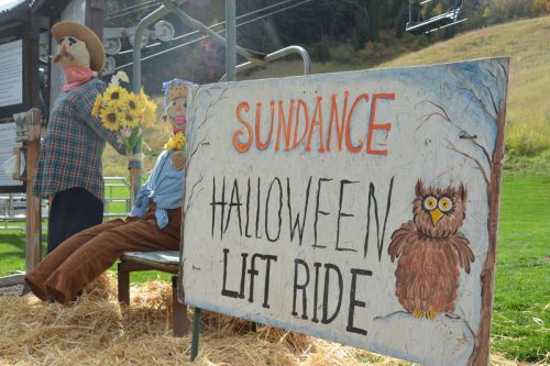 A sign for the Sundance Halloween Lift Ride, with scarecrows sitting on a bench nearby.