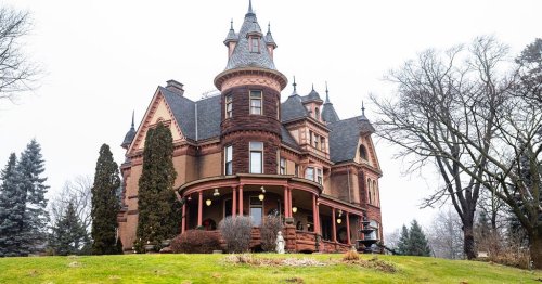 A large, ornate Victorian mansion with turrets and a wraparound porch, surrounded by trees and a grassy lawn.