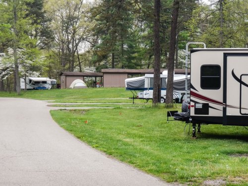 A scenic campground with RVs and tents set up among trees, featuring a paved road and grassy areas.