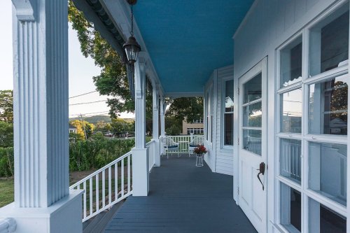 A porch with white railings and blue ceiling, featuring a view of greenery and distant hills.