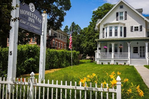 A charming white inn with a sign, surrounded by green grass and yellow flowers, under a blue sky with fluffy clouds.