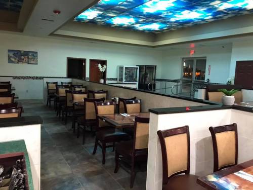 Interior of a restaurant featuring empty tables, chairs, and a colorful ceiling design. Soft lighting creates a cozy atmosphere.