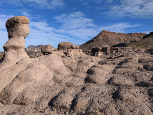Rock formations with unique shapes under a blue sky, featuring a prominent tall column and textured ground.