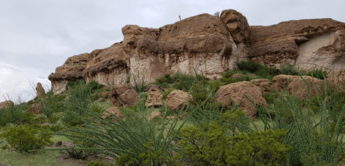 Rocky landscape with rugged cliffs and green vegetation under a cloudy sky.