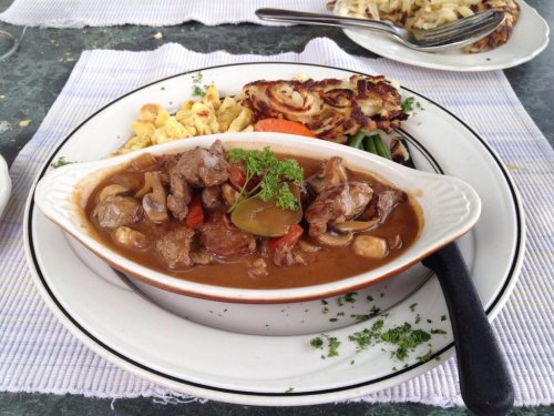 A plate of beef stew with mushrooms, served with vegetables and a side of pasta, garnished with parsley.