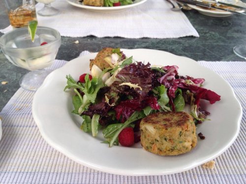A plate with a fresh salad, mixed greens, raspberries, and two round vegetable patties.