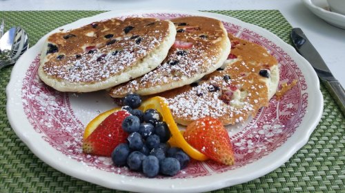 A plate of fluffy pancakes topped with powdered sugar, served with fresh strawberries, blueberries, and orange slices.