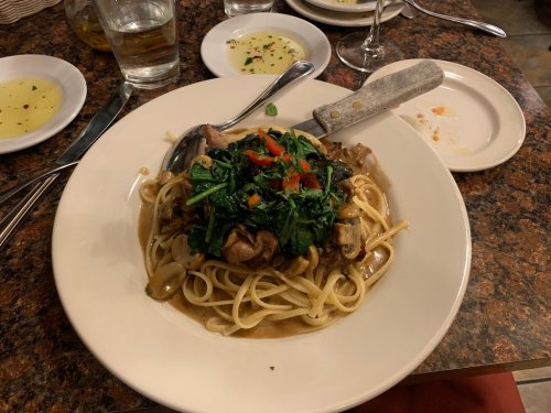 A plate of linguine topped with sautéed greens, mushrooms, and diced tomatoes, served on a rustic table.