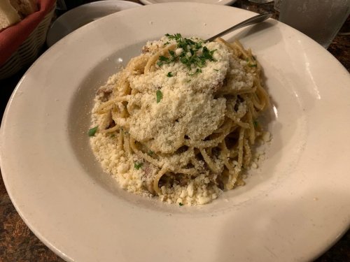 A plate of spaghetti topped with grated cheese and parsley, served in a white bowl on a rustic table.
