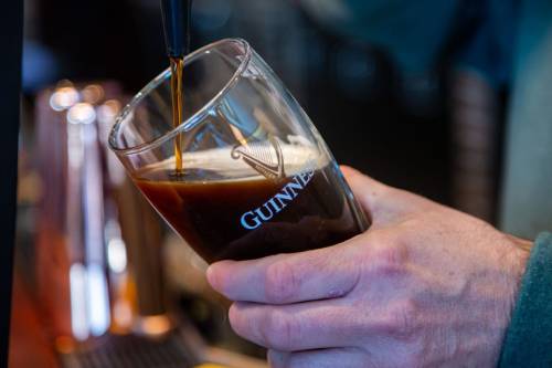 A hand pours dark beer into a Guinness-branded glass at a bar.