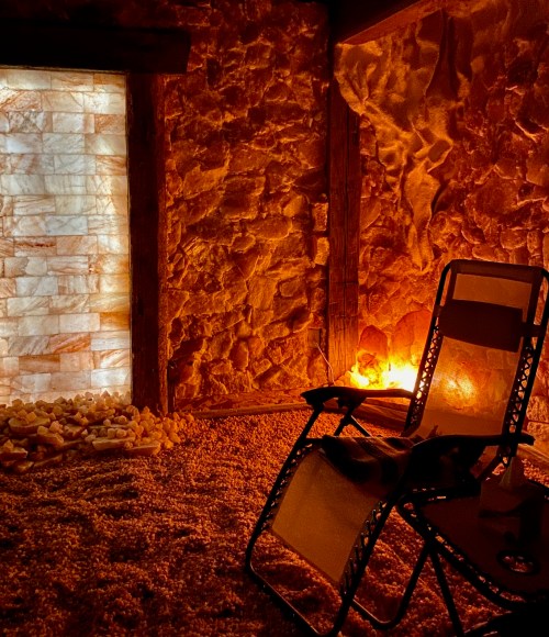 A cozy salt room with a chair, illuminated by warm light and surrounded by salt walls and a salt floor.