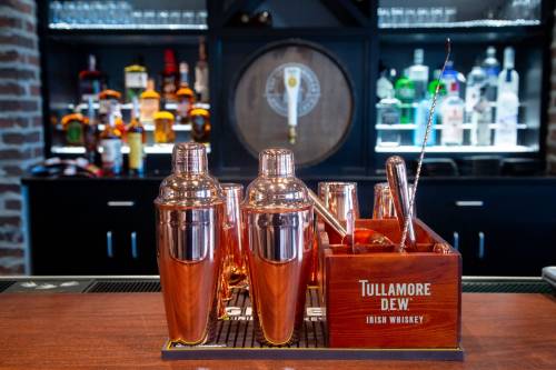 A wooden bar display featuring copper cocktail shakers and a Tullamore Dew whiskey box, with bottles in the background.