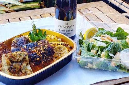 A meal featuring grilled chicken, corn, and a salad, accompanied by a bottle of Chanson Bourgogne Pinot Noir.