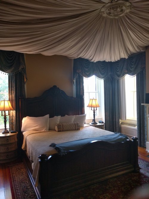 Cozy bedroom with a large bed, decorative drapery, and two lamps, featuring warm colors and a classic design.