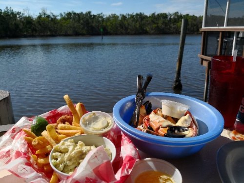 A seafood meal with shrimp, fries, and dipping sauces, set by a scenic river view on a sunny day.