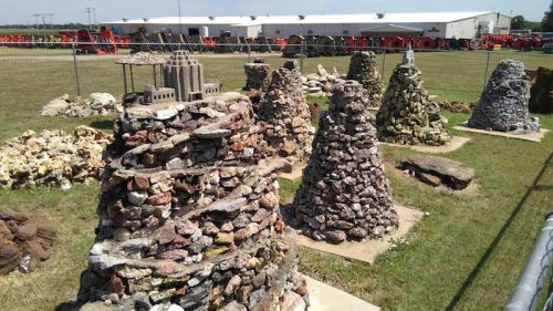 A collection of stone structures resembling small towers, set in a grassy area with buildings in the background.