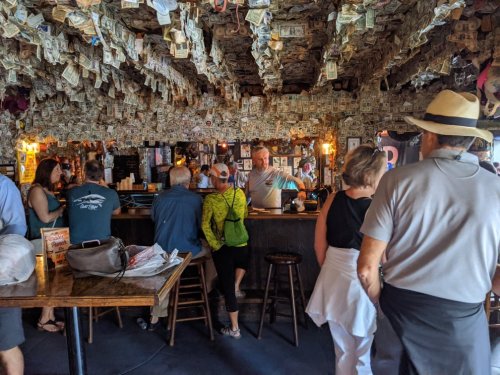 A lively bar interior with a ceiling covered in dollar bills, patrons chatting and enjoying the atmosphere.