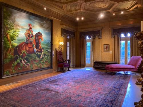 A lavish room featuring a large painting of a man on a horse, ornate decor, and a pink chaise lounge.