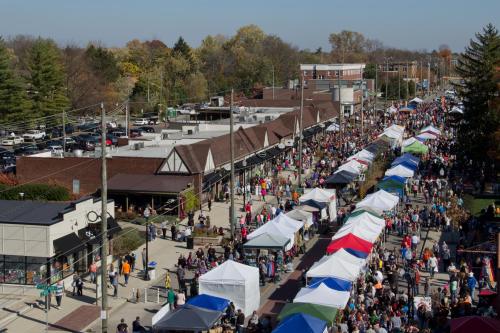 A bustling street fair with numerous tents, vendors, and crowds of people enjoying a sunny day in a vibrant town.