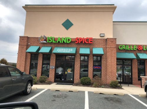 Exterior of Island Spice restaurant featuring a sign for Jamaican cuisine, with a gray car parked in front.