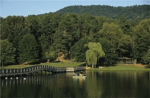 A serene lake surrounded by trees, with a wooden dock and a person in a small boat enjoying the peaceful scenery.