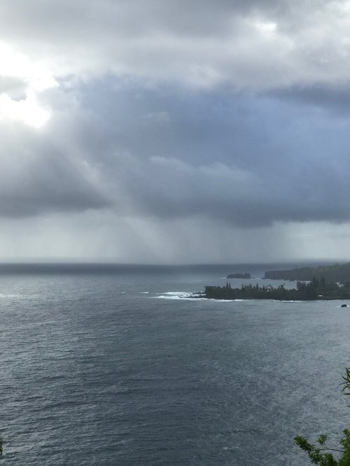 A coastal view with dark clouds and rays of sunlight breaking through, illuminating the ocean and distant land.