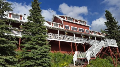 A large red building with white trim and balconies, surrounded by green trees and a blue sky with clouds.