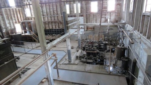 Interior of an industrial building with machinery, pipes, and wooden beams, showing signs of wear and age.